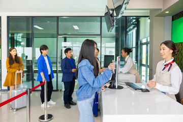 Different ages and nationalities passengers standing in queue to check in at airport terminal. Young asian woman showing flight ticket to staff on phone and waiting for her boarding pass...