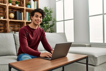 Fototapeta premium Young hispanic man using laptop sitting on the sofa at home.