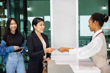 Female flight attendants explaining something to tourist at check-in counter during registration process at international airport terminal.