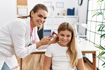 Woman and girl doctor and patient examining ear using otoscope at clinic