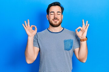 Handsome caucasian man with beard wearing casual striped t shirt relax and smiling with eyes closed doing meditation gesture with fingers. yoga concept.