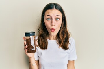 Young brunette woman holding soluble coffee scared and amazed with open mouth for surprise,...