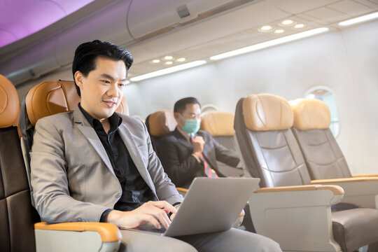 Young Asian Businessman In Formal Wear Using Laptop Computer In Airplane . Business Trip Travel Concept