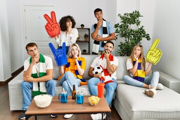 Group of friends supporting football team watching tv al home sitting on the sofa serious face...