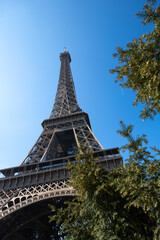 vue sur la tour Eiffel à travers les arbres du Champs de Mars, à Paris en France. Beau ciel bleu et soleil qui apparaît entre les feuilles