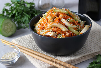 Salad with squid, carrots and cucumber, sprinkled with sesame seeds, in a dark bowl on a light background