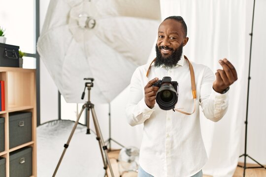 African american photographer man working at photography studio doing money gesture with hands, asking for salary payment, millionaire business
