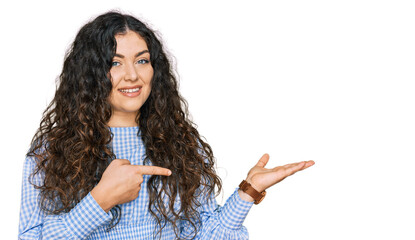 Young hispanic girl wearing casual clothes amazed and smiling to the camera while presenting with hand and pointing with finger.