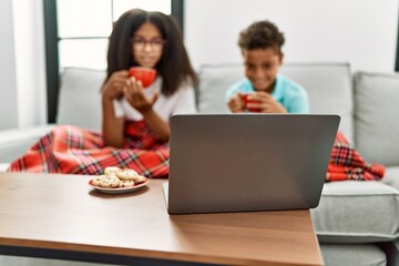 Brother and sister having breakfast watching movie sitting on sofa at home