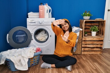 Young hispanic woman doing laundry doing frame using hands palms and fingers, camera perspective