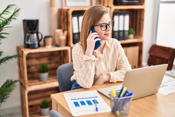 Young blonde woman business worker using laptop and talking on the smartphone at office