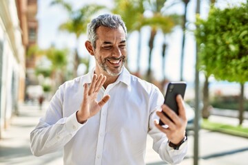 Middle age grey-haired man doing video call using smartphone at the city.