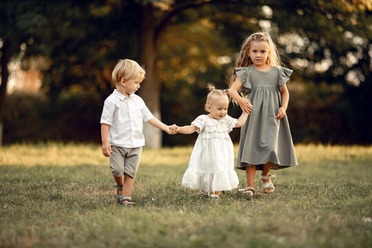 three small children with blond hair are walking together in park, holding the handle. Big family, support, motherhood and love. concept of happy childhood, games, fun. Family leisure. outdoor play