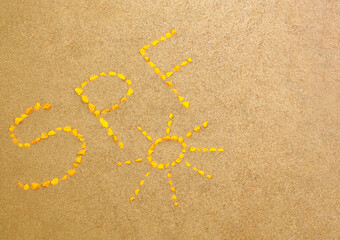 SPF letters written by yellow stones on the sand. Sun protect factor skin care concept background with copy space