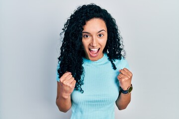 Young hispanic woman with curly hair wearing casual blue t shirt celebrating surprised and amazed for success with arms raised and open eyes. winner concept.