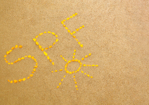 SPF letters written by yellow stones on the sand. Sun protect factor skin care concept background with copy space