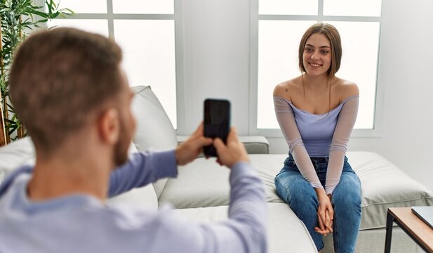 Young man making picture of his girlfriend using smartphone at home.