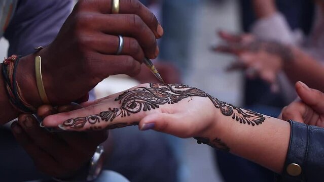 Street artist decorating a woman hand with henna tattoo traditional technique.