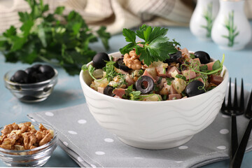 Salad with ham, pineapple, black olives and walnuts in a white bowl on a light blue background