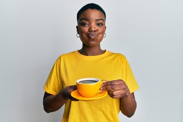 Young african american woman holding coffee puffing cheeks with funny face. mouth inflated with air, catching air. - obrazy, fototapety, plakaty