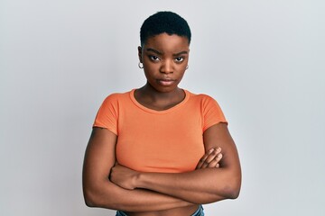 Young african american woman wearing casual orange t shirt skeptic and nervous, disapproving expression on face with crossed arms. negative person.