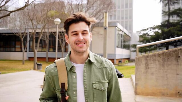 Close up shot of cheerful happy caucasian teenage boy looking at camera smiling. Funny portrait of a young student man with his backpack at campus university. Guy laughing at high school.