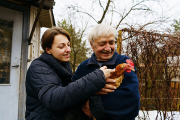 Grandfather and granddaughter hold a chicken in their hands and smile standing on the farm