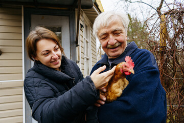 Grandfather and granddaughter hold a chicken in their hands while standing on the farm