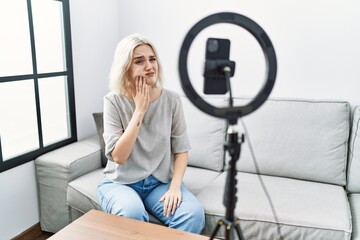 Fototapeta na wymiar Young caucasian woman recording vlog tutorial with smartphone at home touching mouth with hand with painful expression because of toothache or dental illness on teeth. dentist