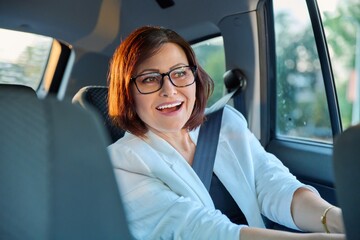 Fototapeta na wymiar Portrait of business elegant middle-aged woman in car in back passenger seat
