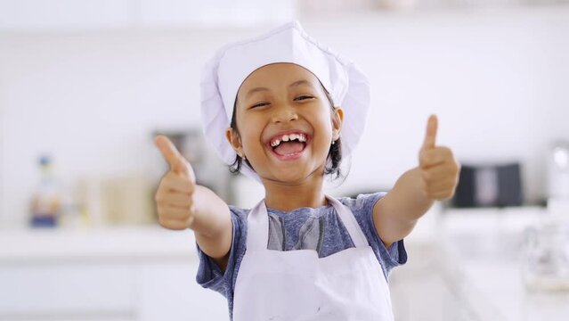 Cheerful little girl showing thumbs up in kitchen