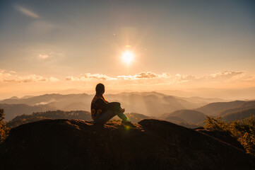 Silhouette young hiker woman relaxing and enjoying the sunset view on top of mountain peak at...