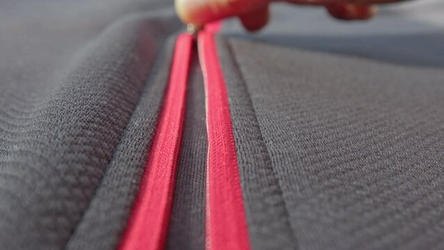 Extreme close up zipper with hand unzipping the sweater jacket zipper while camera following the man hand. Fashion, textile and clothing industry concept.
