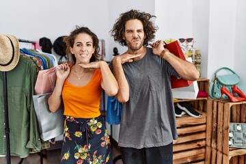 Young hispanic couple holding shopping bags at retail shop cutting throat with hand as knife, threaten aggression with furious violence