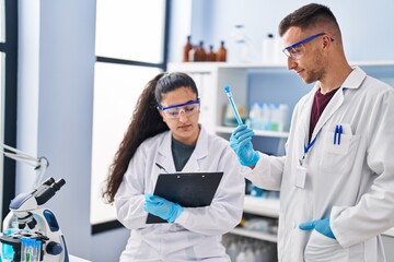 Man and woman wearing scientist uniform write on clipboard holding test tube at laboratory