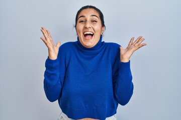 Fototapeta premium Young hispanic woman standing over isolated background celebrating crazy and amazed for success with arms raised and open eyes screaming excited. winner concept