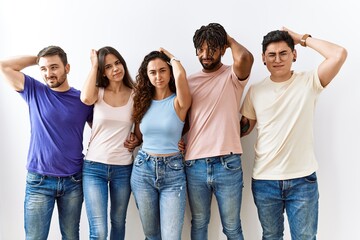 Obraz premium Group of young people standing together over isolated background confuse and wondering about question. uncertain with doubt, thinking with hand on head. pensive concept.