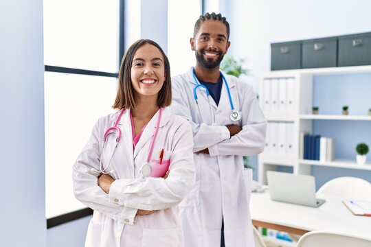 Man and woman wearing doctor uniform smiling confident standing with arms crossed gesture at clinic