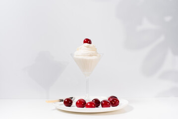Helado de crema con cerezas sobre una mesa blanca. Sombras suaves de hojas en la pared postre de verano