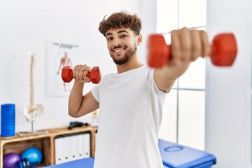 Young arab man patient doing rehab using dummbells at clinic