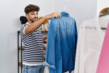 Young arab man customer holding shirt shopping at clothing store