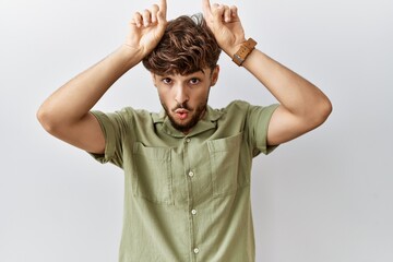 Young arab doctor man standing over isolated background doing funny gesture with finger over head as bull horns