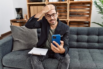 Young hispanic psychologist man doing therapy on video call with smartphone stressed and frustrated with hand on head, surprised and angry face