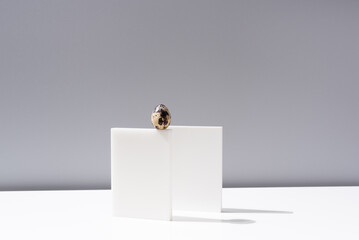 Un huevo de codorniz sobre un soporte blanco y fondo gris