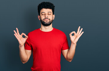Naklejka premium Young arab man with beard wearing casual red t shirt relax and smiling with eyes closed doing meditation gesture with fingers. yoga concept.