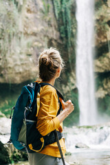 Young active unrecognizable woman from behind with a backpack looking at a waterfall in a canyon.