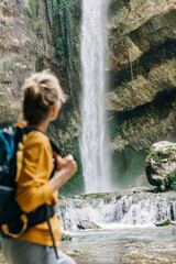 Defocused unrecognizable woman from behind with a backpack looking at a waterfall in a canyon.