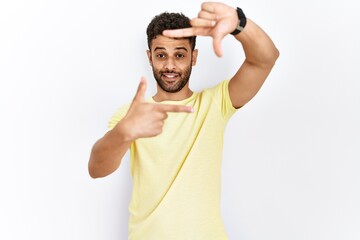Arab young man standing over isolated background smiling making frame with hands and fingers with happy face. creativity and photography concept.