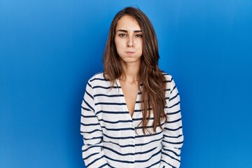 Fototapeta premium Young hispanic woman standing over blue isolated background puffing cheeks with funny face. mouth inflated with air, crazy expression.