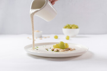 Verter crema de almendras, sopa fría española. Ajo blanco de Málaga con almendras y uvas en un recipiente blanco sobre una mesa blanca
